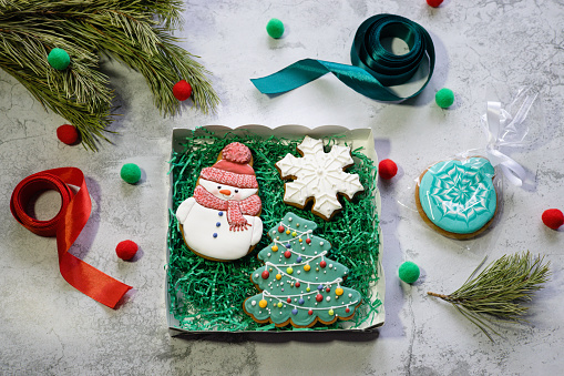 Gingerbreads in the form of snowman, Christmas tree and snowflake in gift box next to pine branch and ribbons. Preparing of Christmas gifts. Winter holidays concept.