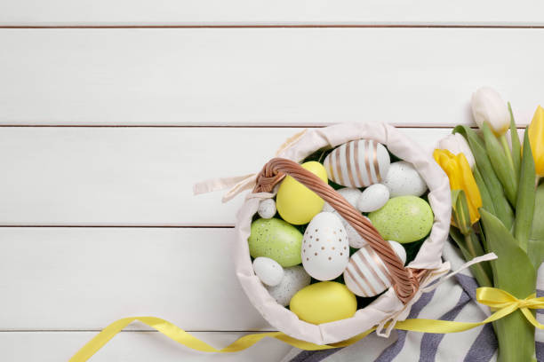 huevos de pascua en cesta y tulipanes sobre mesa de madera blanca, planos. espacio para el texto - picnic basket christianity holiday easter fotografías e imágenes de stock