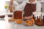 Woman decorating traditional Easter cake with glaze at white marble table in kitchen, closeup