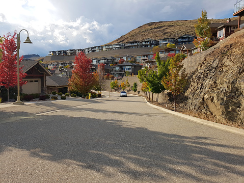 Residential Street with tree lined Autumn colors. Car at end of road. House above.