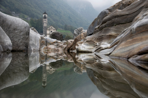 Church and rocks mirrored in water in the swiss mountains.