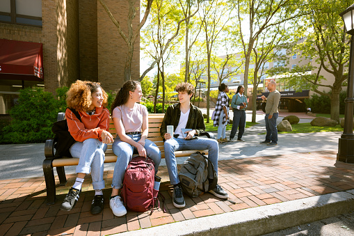 University students wait for the bus sitting on a bench in campus