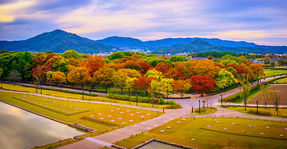 Gyeongju City Historic Site, vibrant autumn foliage, crossing footpaths, and dramatic cloudscape over Namsan Mountains at Wolseong District along Namcheon or South River, South Korea