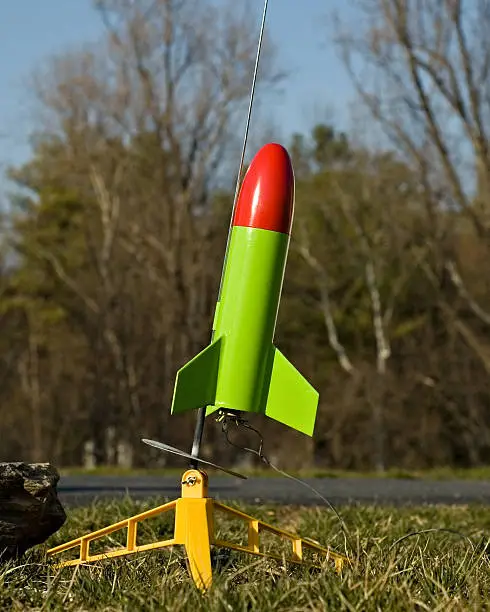 "Toy rocket perched on pad, wired and ready to launch. DOF focus on rocket with deemphasized trees in background."