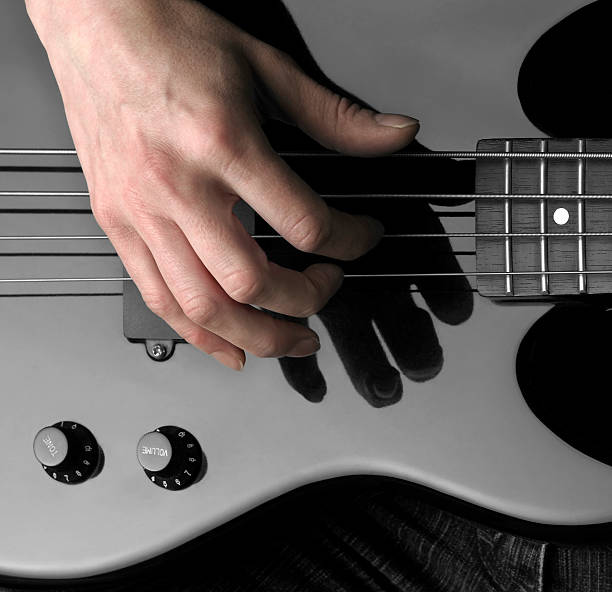 electric bass and hand hand on the detail of a black bass guitar in dark back regler stock pictures, royalty-free photos & images
