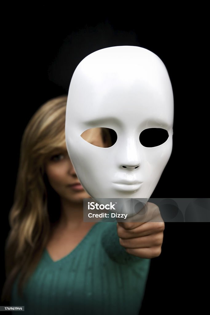 Behind the mask. Young woman with her face partially obscured by a blank white mask. Behind Stock Photo