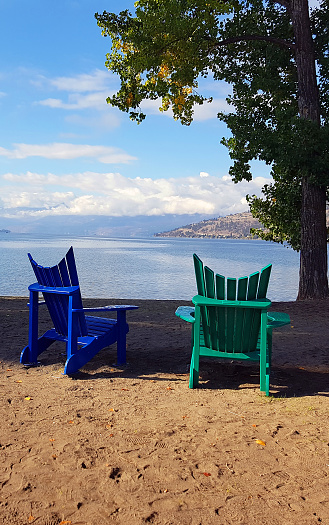 Looking over Lake Okanagan from Kin Beach Vernon BC.  Two Adirondack Chairs on Sand.