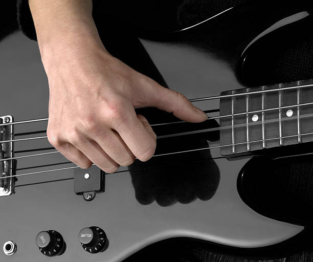 bass guitar and hand detail of a black bass guitar and female hand  in dark back regler stock pictures, royalty-free photos & images