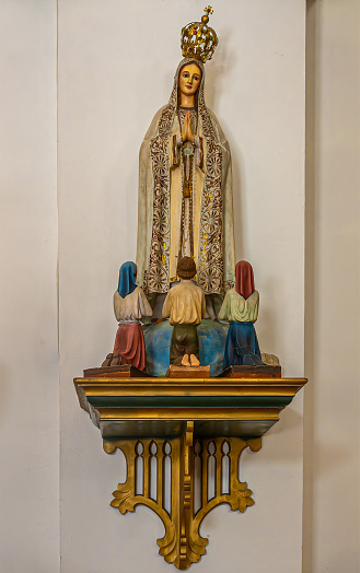 Guatemala, La Antigua - July 20, 2023: San Jose Cathedral. \nStatue of Virgin Mary at her apparition in Fatima before 3 children. Beige wall in back. Golden trim