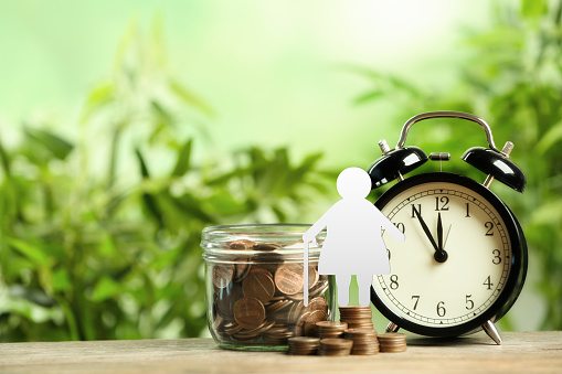 Pension concept. Elderly woman illustration, coins and alarm clock on wooden table. Space for text