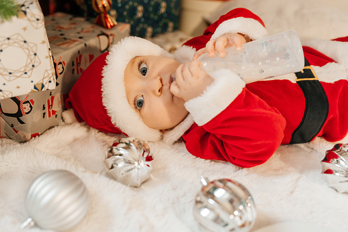 Beautiful little baby boy celebrates Christmas. New Year's holidays. Baby in a Christmas costume Santa's clothes with gifts on fur close to new year tree.