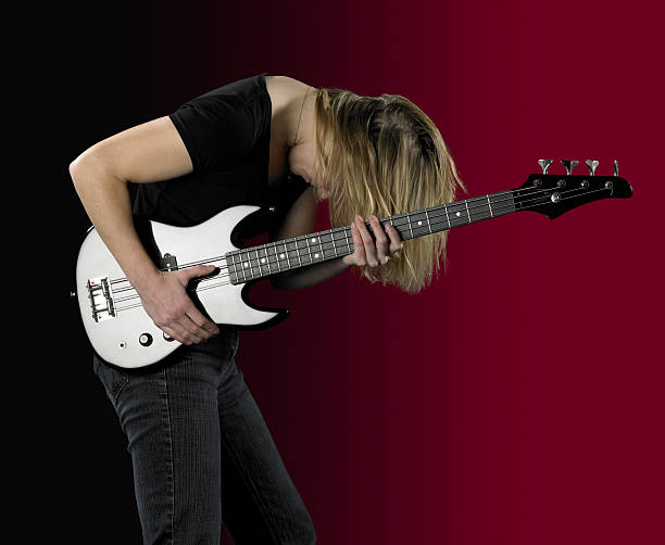 blonde girl and electric bass  a woman and a reflective black bass guitar in front of partly reddish back regler stock pictures, royalty-free photos & images