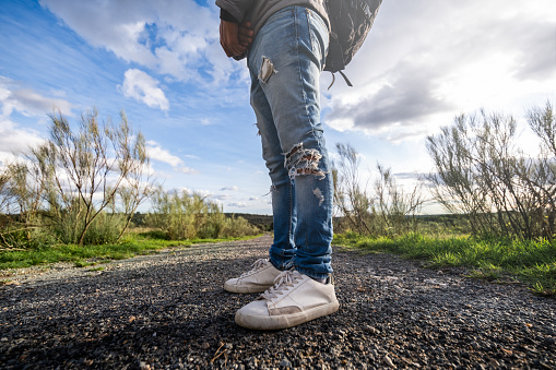 Unidentifiable young man's legs in ripped jeans and white casual sneakers, forest background.