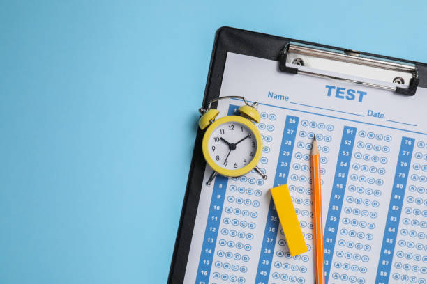 istock Student passing exam. Clipboard with answer sheet, pencil and alarm clock on light blue background, top view. Space for text. 1769634974