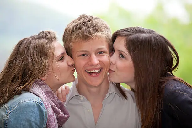 Photo of smiling teenager being kissed by teenage girls