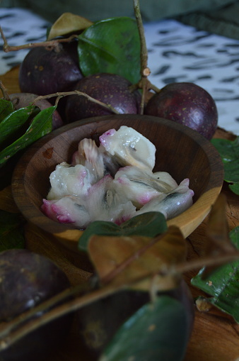 A delicious purple Abiu fruit cut in the wooden pot served alongside whole fruits and green leaves