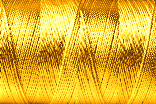 Spool of golden sewing thread as background, closeup