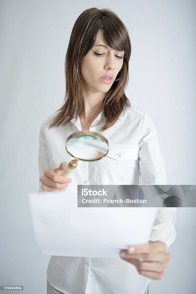 Document scrutiny ..Young woman inspecting closely a document through a magnifying glass.. 20-24 Years Stock Photo
