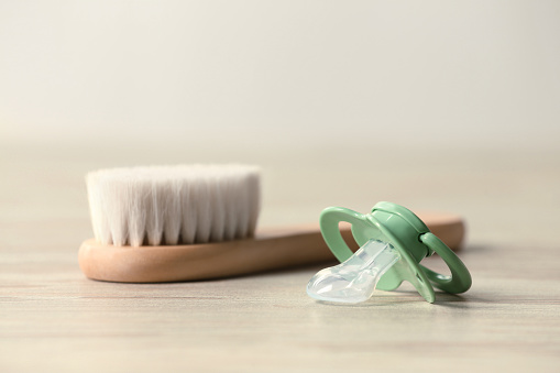 Baby pacifier and hairbrush on beige table against blurred background