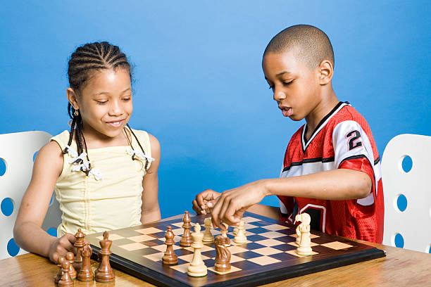 garçon et fille jouant aux échecs - little girls fun lifestyle handcarves photos et images de collection