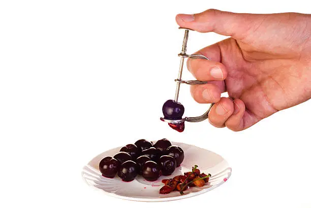 Cherry pitter in hand and cherries on plate