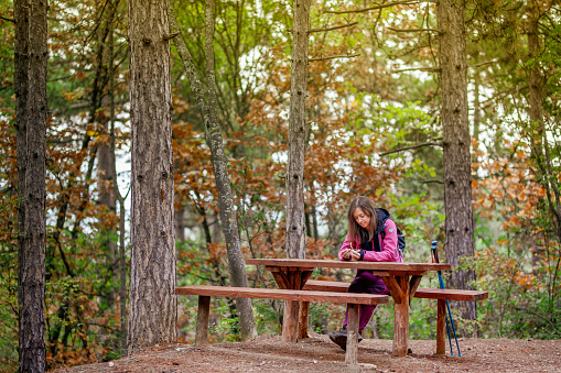 Hiker girl resting on a bench in the forest. Backpacker with pink jacket in nature.