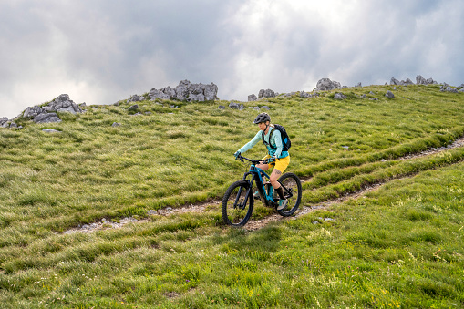 Woman riding electric mountain bike at green meadows landscape wide shot