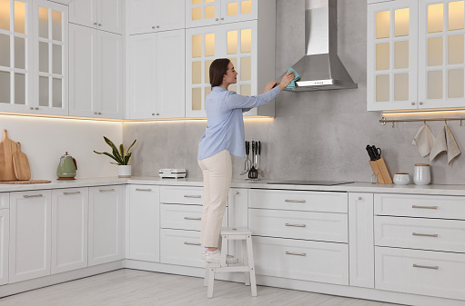 Woman on ladder wiping kitchen hood at home