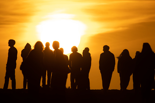 Silhouettes of people standing on a hill at a bright orange sunset. Mid shot