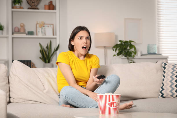istock Surprised woman watching TV with popcorn on sofa at home 1769745915