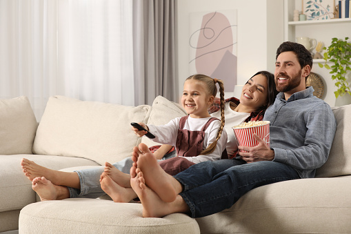 Happy family watching TV with popcorn on sofa at home