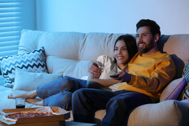istock Happy couple watching TV with pizza on sofa indoors 1769756512