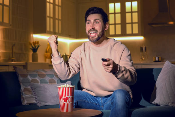 istock Excited man watching TV with popcorn on sofa at home 1769758117