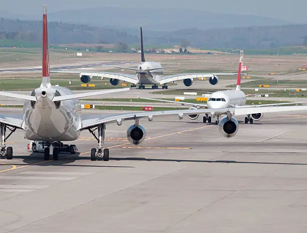 Three passenger aircrafts in heavy traffic on the taxiway of Zurich international airport. Aircraft types on picture include  Airbus A380 (middle). Two moving away, one approaching. Looks like the aircrafts are deadlocked in a taxiway traffic jam.