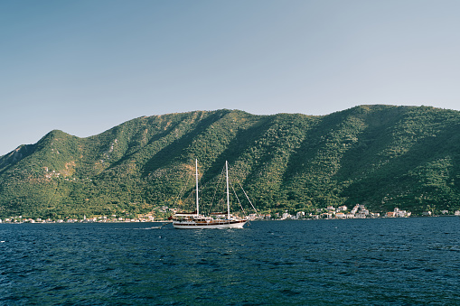 Sailing yacht sails on the blue sea along the green mountain range. High quality photo