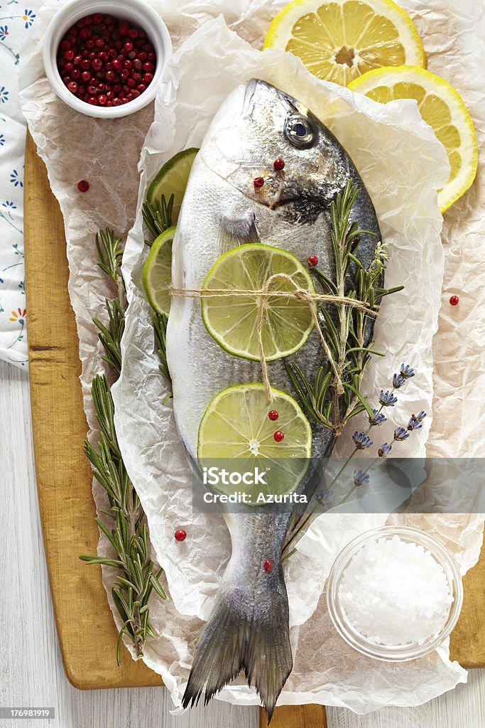 Raw dorado "Fresh sea bream with lemon, lime, rosemary, salt and pink pepper on wooden cutting board and paper wrapping" Close-up Stock Photo