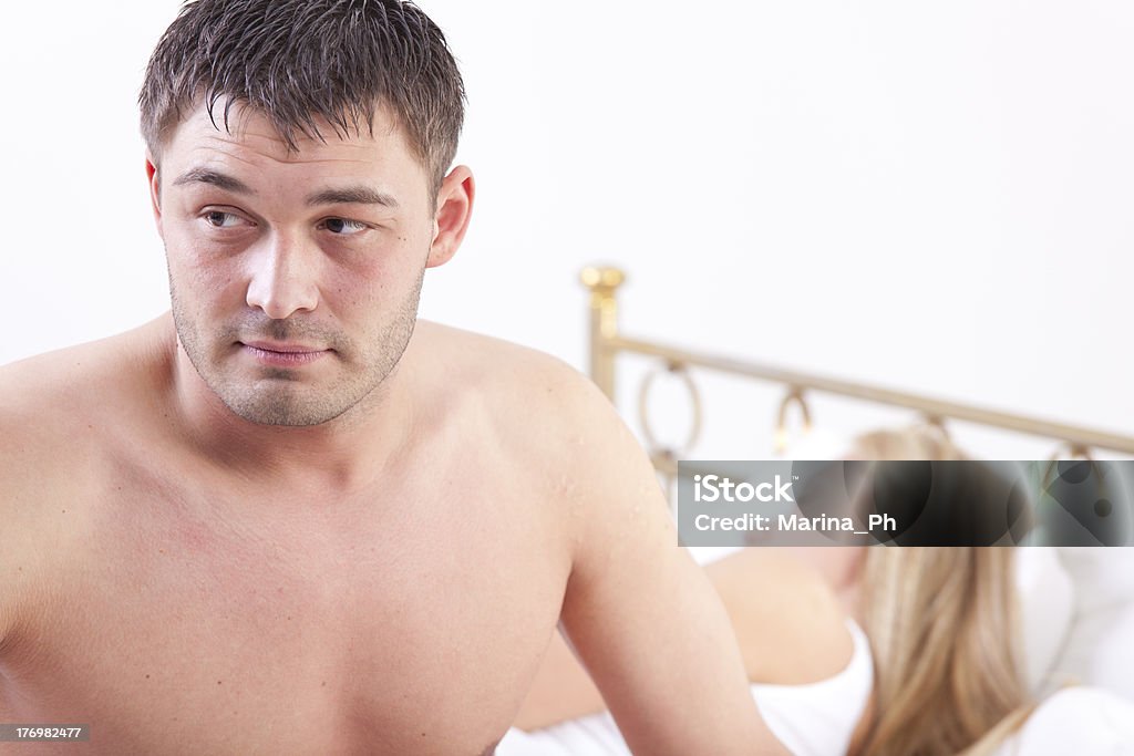 Couple with problems worried man sitting on bed - woman sleeping in background 20-29 Years Stock Photo