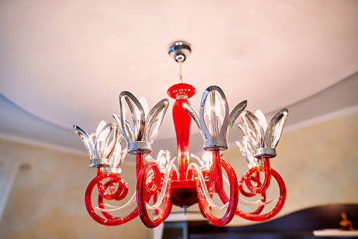 Red chandelier with swirls and flower-shaped shades hangs from the ceiling. High quality photo
