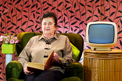 Elderly woman reads the book in her room.