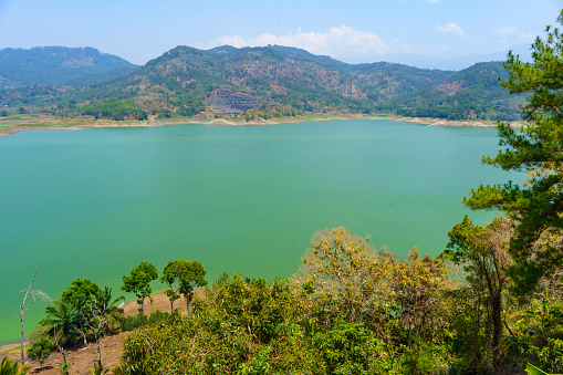 A serene man made lake surrounded by majestic hills, reflecting the blue sky and white clouds above