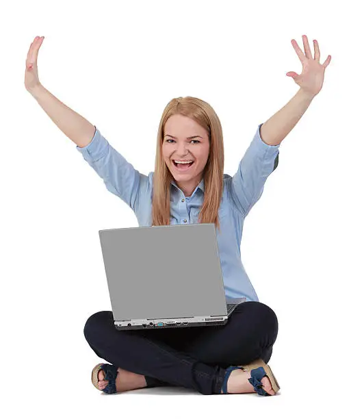 Happy young blonde woman raising hands while sitting with a laptop in her lap.