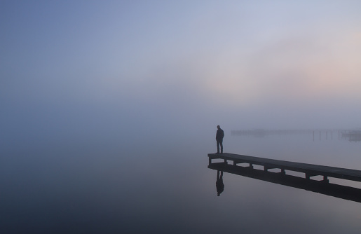 Depressed man standing at the end of a jetty on a foggy day.