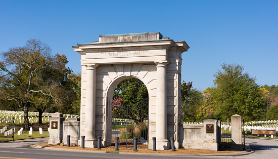 Entry Arch to Nashville National Cemetery, Nashville, Tennessee. Bright sunshine, cloudless blue sky. Headstones visible on either side.
