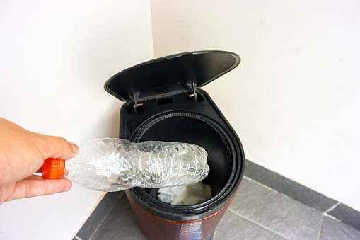 Close up view of human hand throwing an empty plastic bottle into the trash can. Environment care concept, ecological lifestyle, garbage recycle bin, trash sorting
