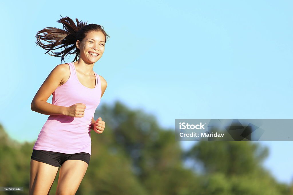 Happy woman running Happy xwoman running in city park. Asian girl runner jogging smiling aspirational outside on beautiful summer day. Mixed race Asian Chinese / Caucasian female fitness sport model training outdoors.Click for more: 20-29 Years Stock Photo