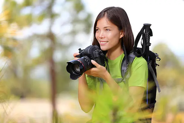 Nature travel photographer xwoman taking pictures in forest during hiking trip. Beautiful happy smiling young xwoman holding professional SLR camera. Mixed race Chinese Asian / Caucasian girl photographing. Click for more :