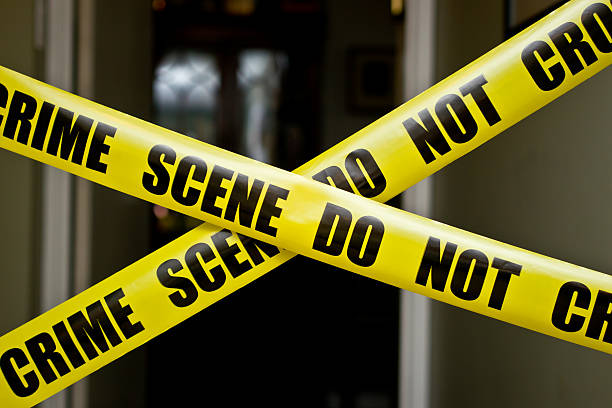 A yellow warning tape with the word CRIME tied to a tree, indicating a crime scene investigation in the woods.