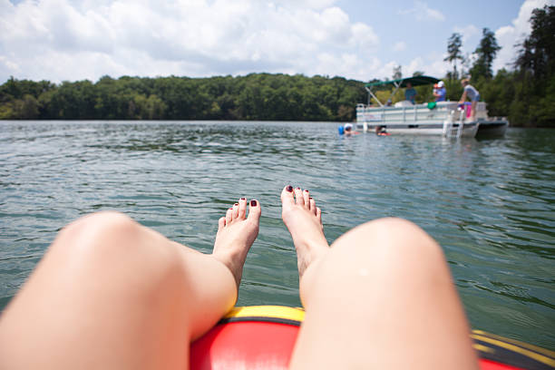 Woman relaxing in tube on lake while looking at pontoon Woman sits in tube relaxing on lake while looking at pontoon pontoon boat stock pictures, royalty-free photos & images