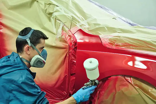 Worker painting a red car in a paint booth.