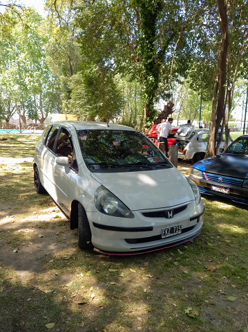 Remedios de Escalada, Argentina - Oct 8, 2023: Old white 2000s Honda Fit five door hatchback on the lawn under the trees at a classic car show in a park